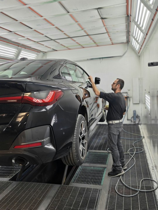 Carrossier bij een zwarte BMW in de spuitkabine